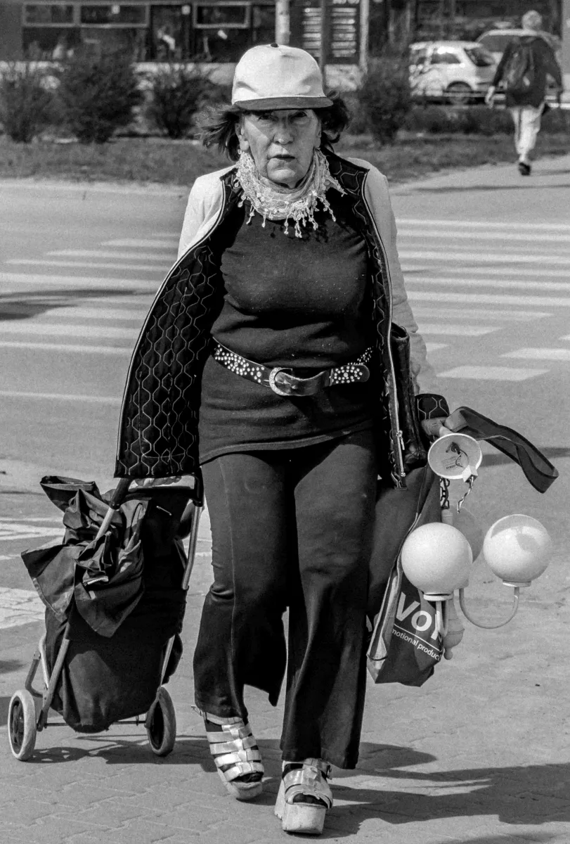 Older woman crossing the street with a shopping trolley and balloons